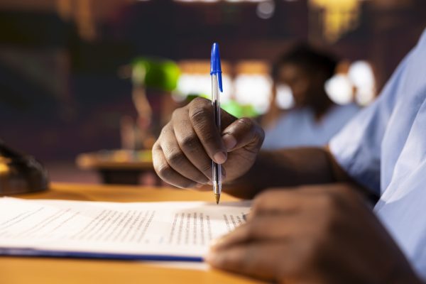 Black male pupil makes notations about practice methods to prepare for an exam, studying at the library to obtain his med school diploma for a medical career. Student does a summary. Close up.
