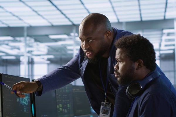 Data center manager helps intern implement AI predictive maintenance systems. Server farm supervisor checks work done by employee using artificial intelligence to identify hardware failures, camera A
